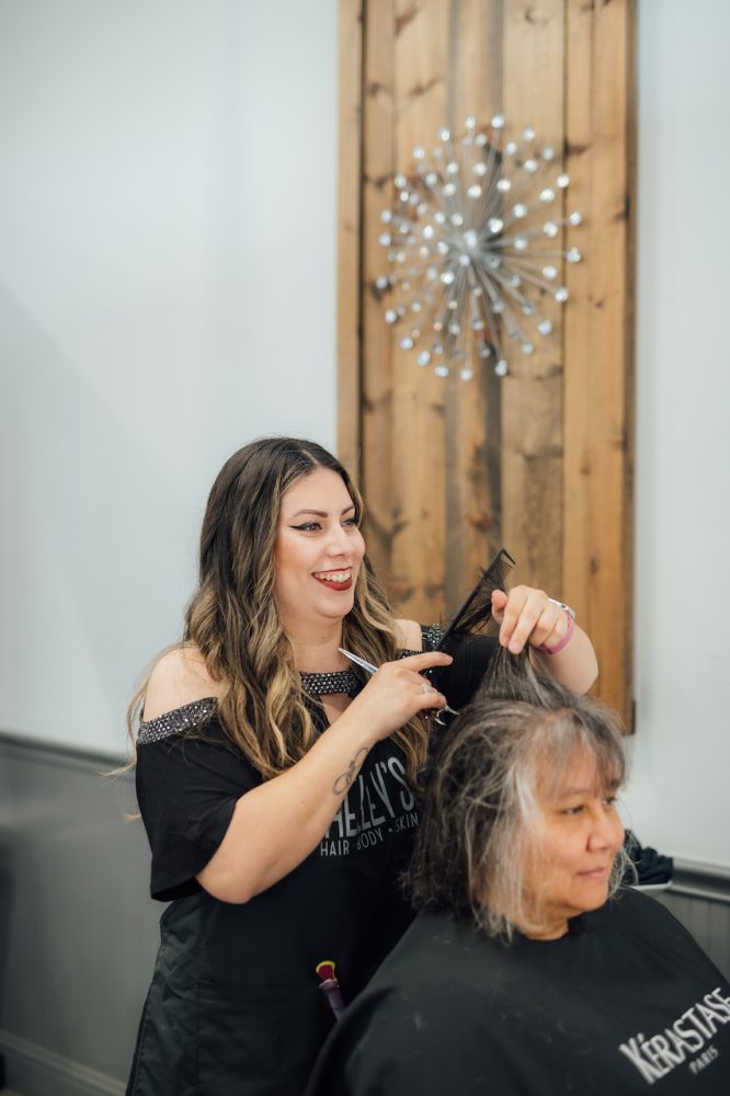 A stylist at Shelley's Hair, Body, and Skin in Belton, TX, smiles as she works with a client getting a hair cut